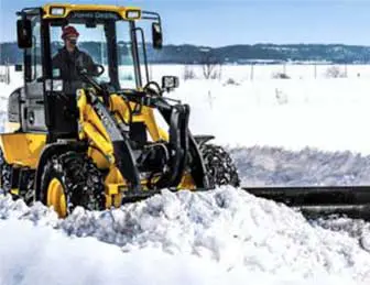2 A person operating a yellow john deere tractor equipped with a snow plow clearing snow.