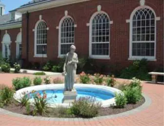 3 Statue overlooking a small circular pool in front of a brick building with arched windows.