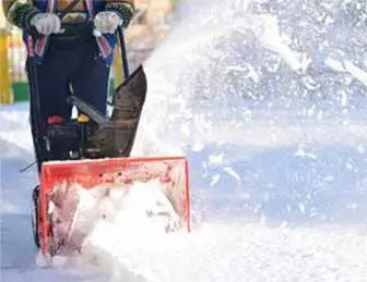 4 Person operating a snowblower to clear snow from a path.
