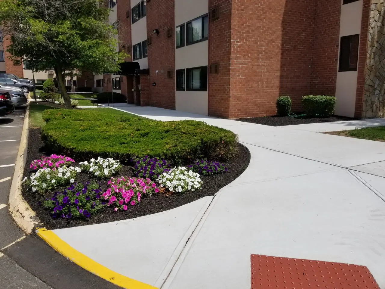 Landscaped garden area with colorful flowers in front of a brick apartment building.