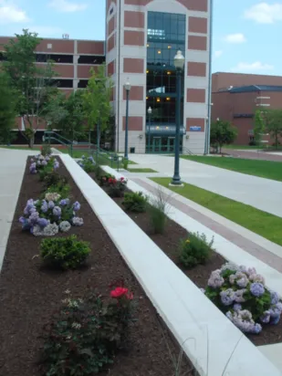 about2 Landscaped pathway with flower beds leading to a modern building.
