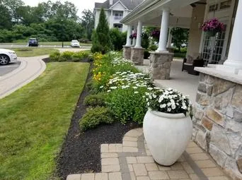 about4 Landscaped front yard with a flower-lined pathway leading to a house with columns and a large decorative planter.